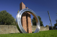 Sculpture with a large metal ring & two brick colums behind